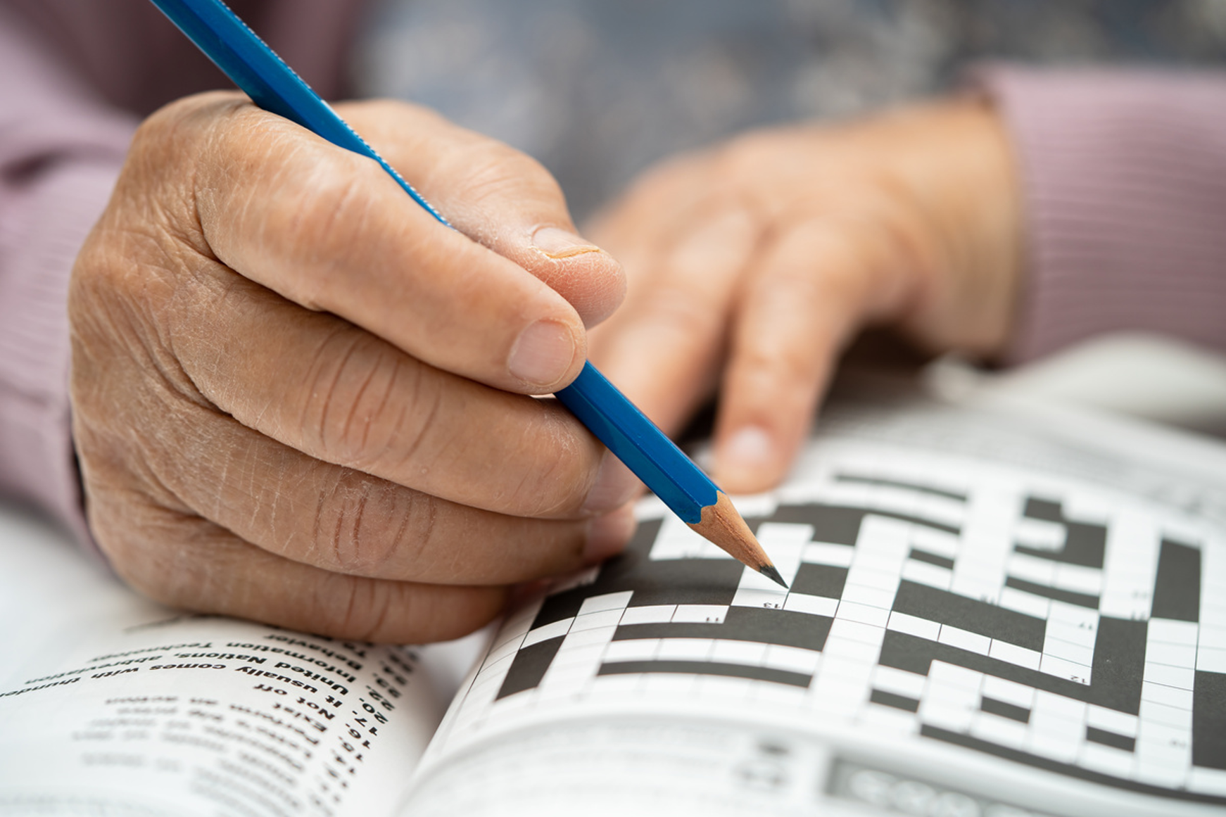 Hands holding pencil over open crossword puzzle book