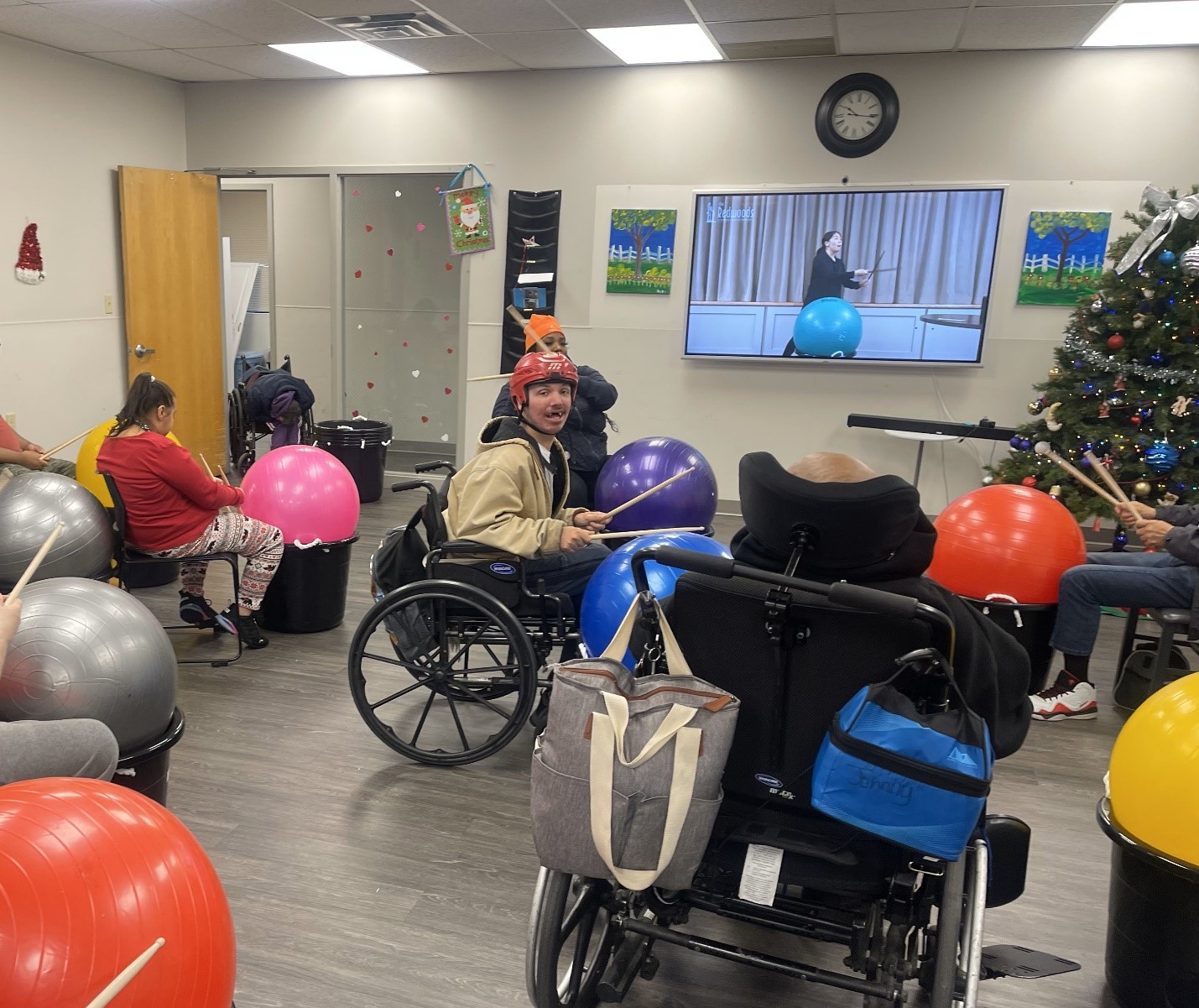 Resident on chairs and wheelchairs do cardio drumming watching along on a Smartboard