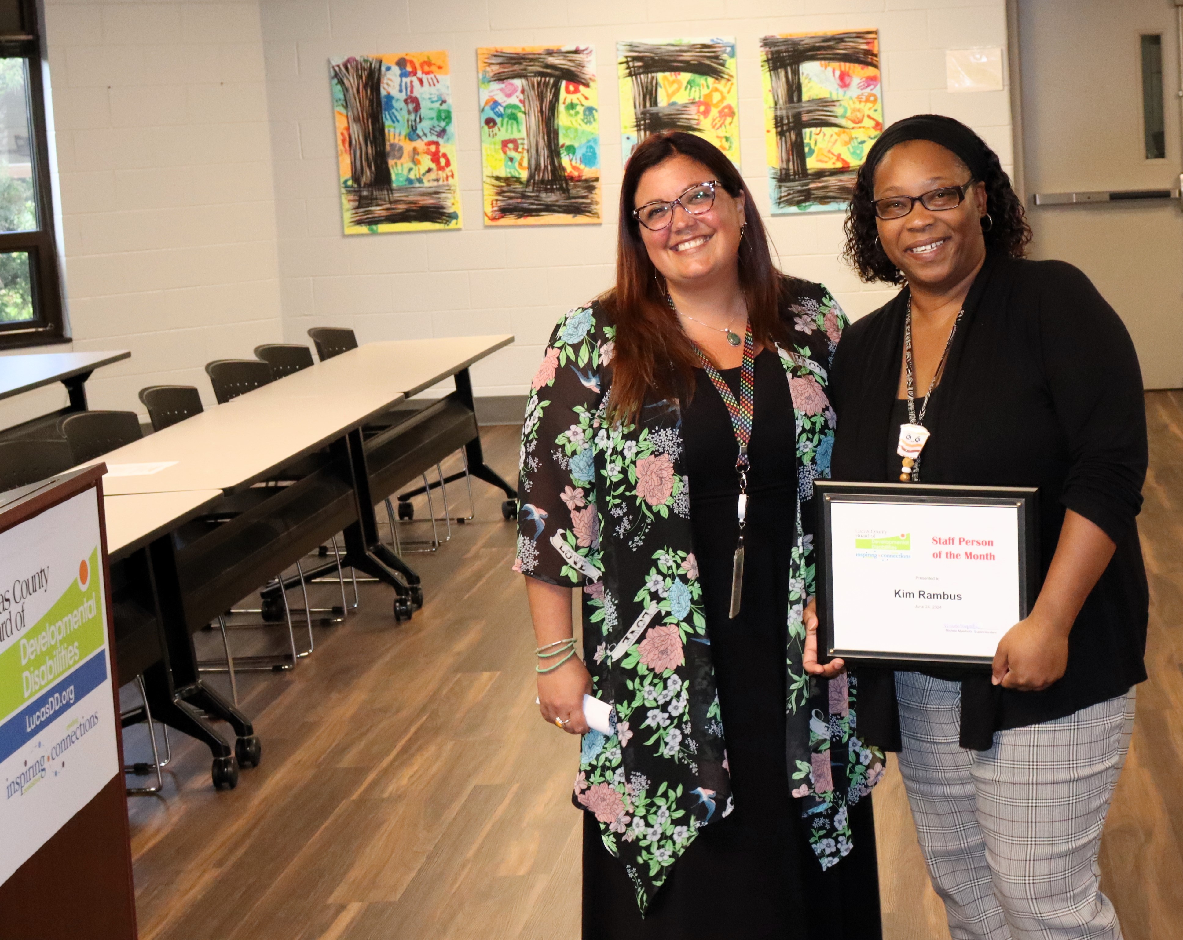 June 2024 Staff Person of the Month Kim Rambus holds her plaque and poses next to SSA Assistant Director Sarah Dodson