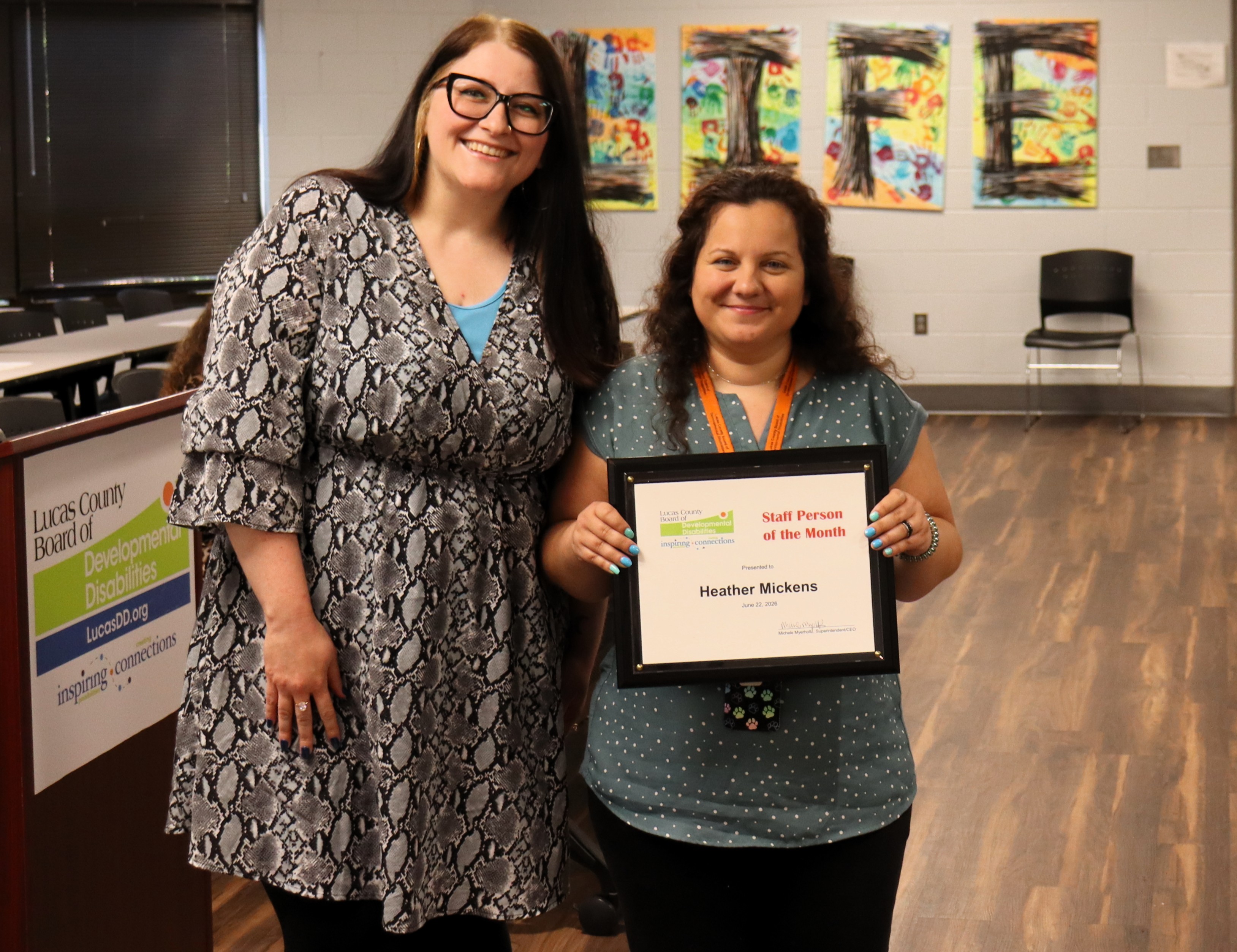 Picture of two females standing side by side. The one on the left is wearing glasses. The one on the right is holding her Staff Person of the Month plaque