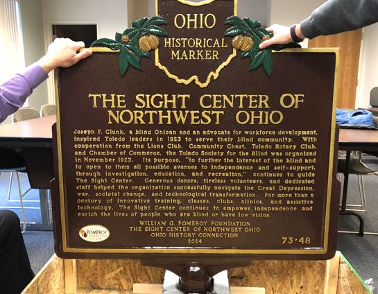 The Sight Center historical marker being held up by two hands