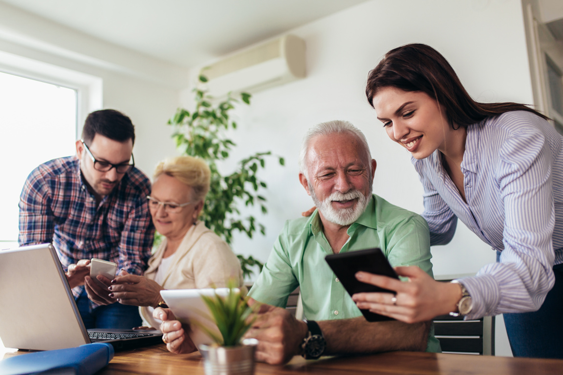 Young man and woman showing older man and woman phone and computer screens.