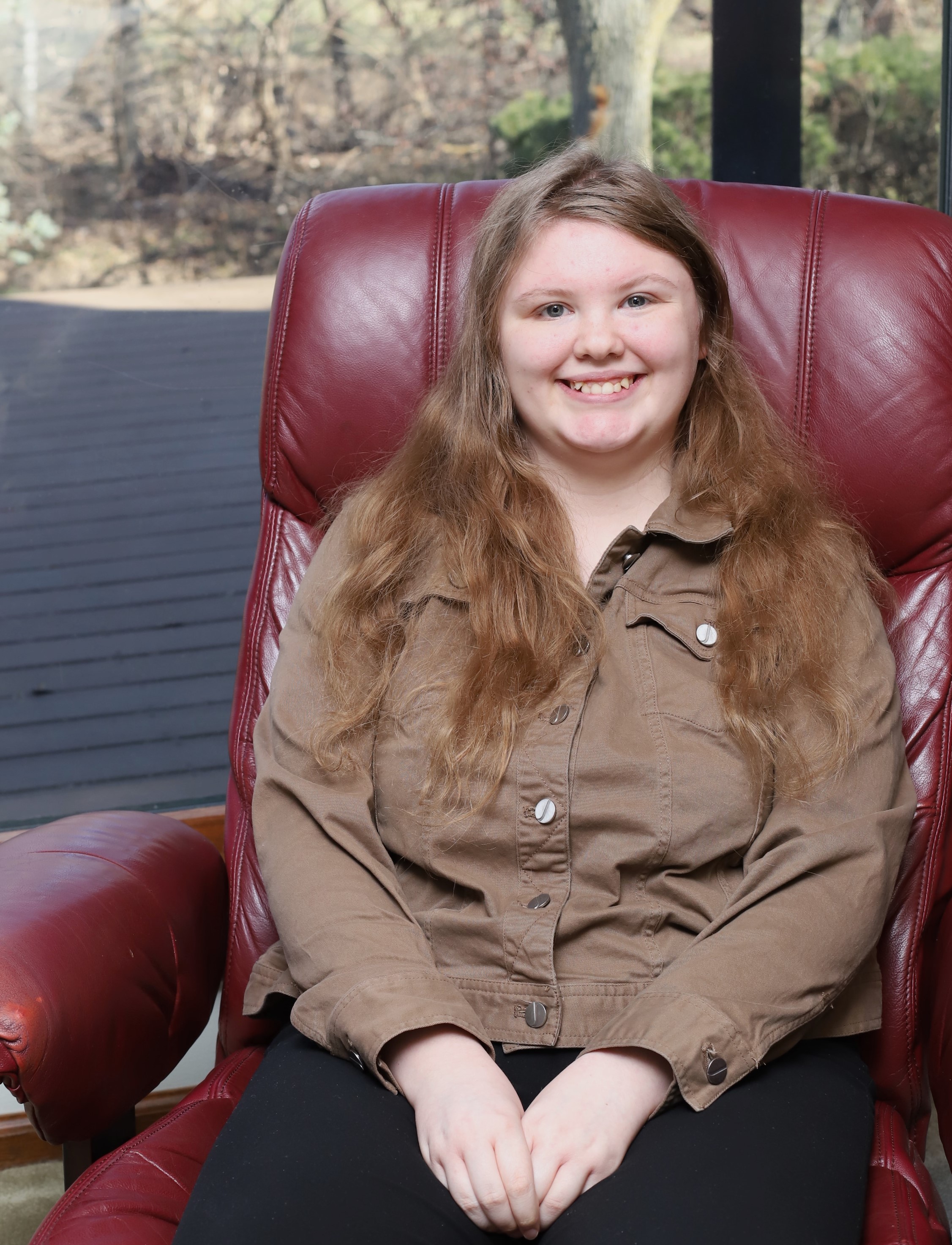 smiling young lady looking a camera with hands in lap