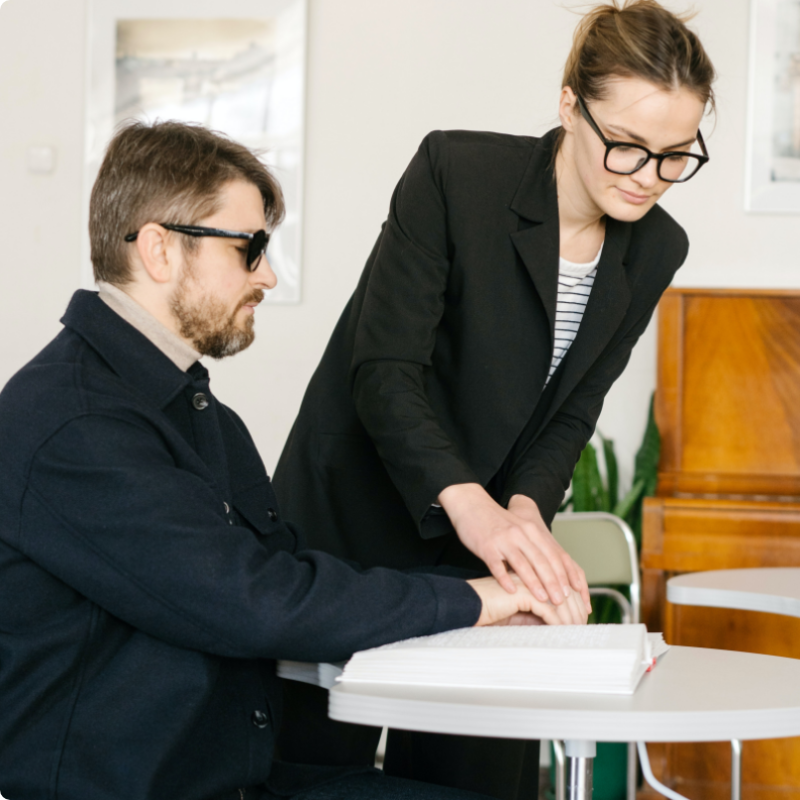 Woman helping man read Braille