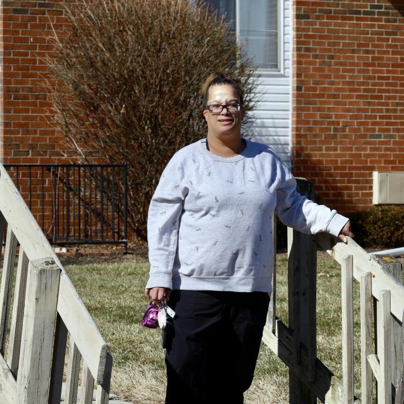 Female individual with dark hair and glasses standing on steps with her hand on a wooden rail