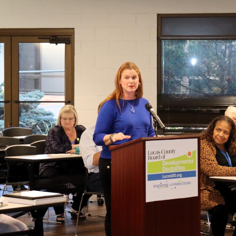 Woman in a blue shirt standing at a podium with the Lucas DD logo in the front