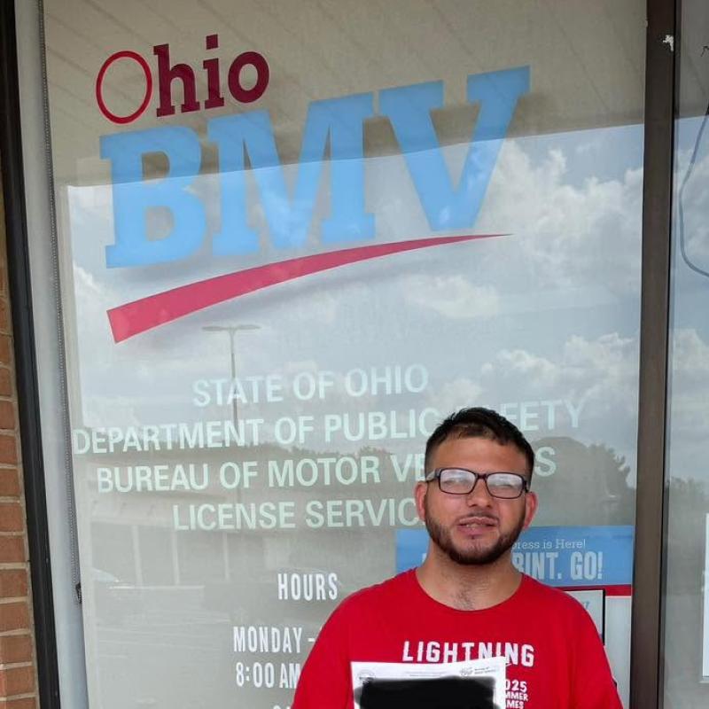 Young man standing in front of the Ohio BMV office holding a certificate