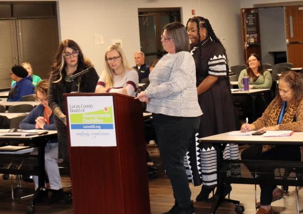 SSA Director Kristin Aemisegger reads the recognition at the podium as she is flanked by 3 femaile employees of Anne Grady Services