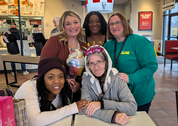 Four ladies standing around a woman who is seated at a table after lunch at KFC